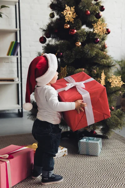 Menino em santa chapéu com caixas de presente perto da árvore de natal — Fotografia de Stock