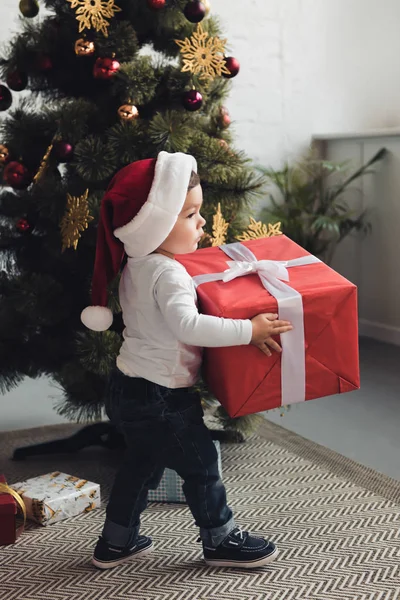 Toddler in santa hat with gift boxes near christmas tree — Stock Photo