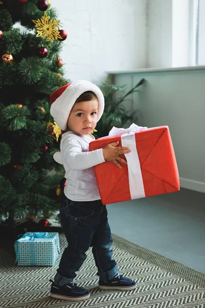 Adorable kid in santa hat with presents near christmas tree — Stock Photo