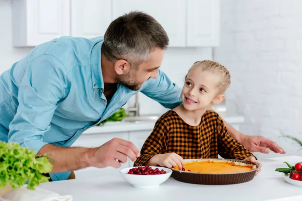 Счастливый отец и очаровательная маленькая дочь украшают тыквенный пирог на День Благодарения вместе — стоковое фото
