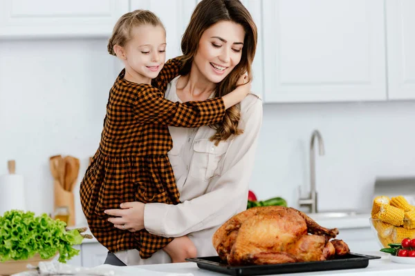 Beautiful young mother and daughter embracing and looking at thanksgiving turkey — Stock Photo
