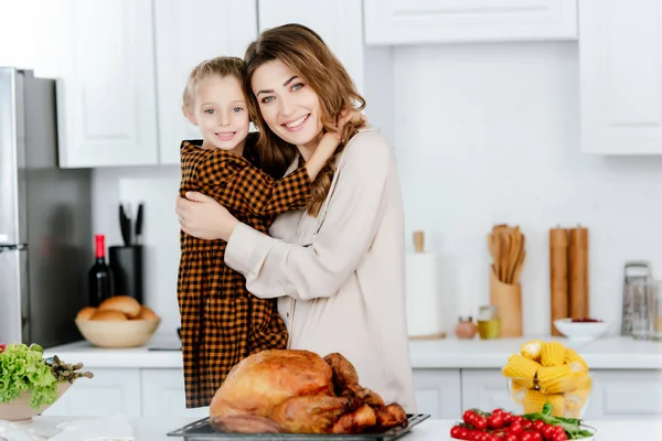 Beautiful young mother and daughter embracing and looking at camera while cooking thanksgiving turkey together — Stock Photo