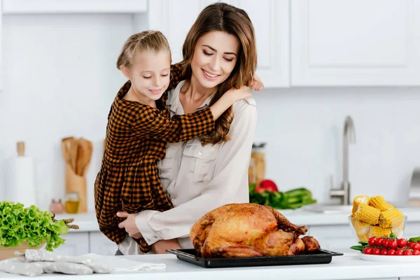Hermosa joven madre e hija abrazando mientras cocinan pavo de acción de gracias juntos - foto de stock