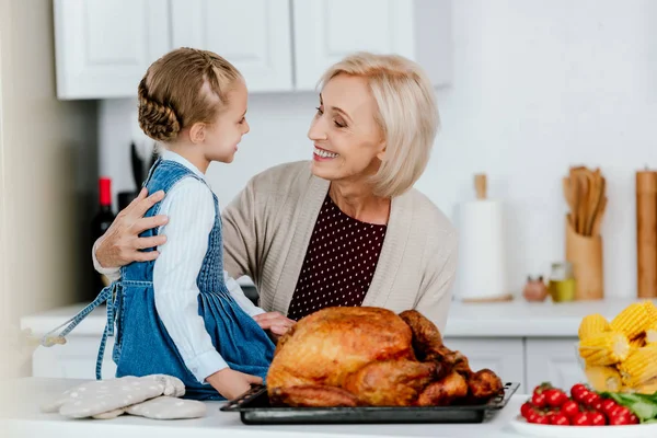 Smiling mature woman preparing thanksgiving turkey with granddaughter — Stock Photo