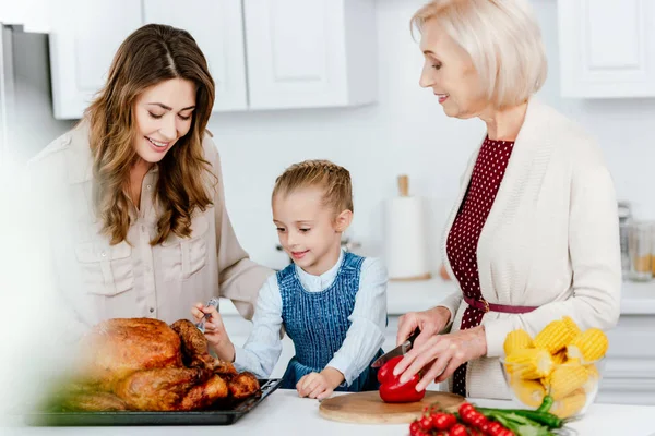 Happy mother and grandmother preparing thanksgiving turkey with granddaughter — Stock Photo