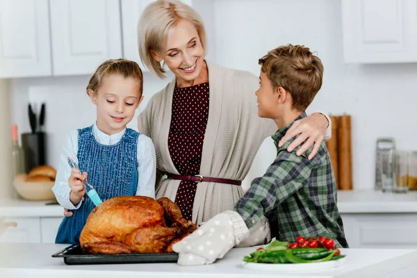 Happy siblings preparing thanksgiving turkey with grandmother at kitchen — Stock Photo