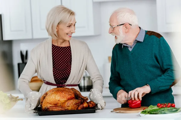 Felice coppia anziana cucinare tacchino Ringraziamento insieme e guardarsi l'un l'altro — Foto stock