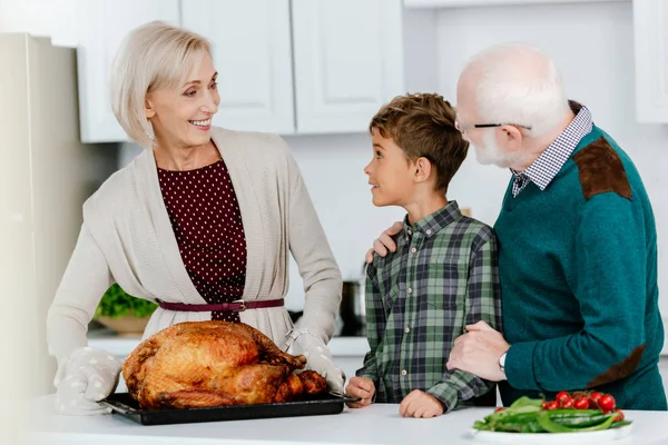 Excited little kid with grandparents preparing thanksgiving turkey together at kitchen — Stock Photo