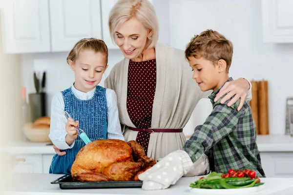 Adorable siblings preparing thanksgiving turkey with grandmother at kitchen — Stock Photo