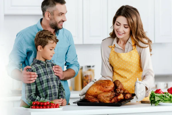 Niño pequeño con los padres preparando pavo de acción de gracias juntos en la cocina - foto de stock