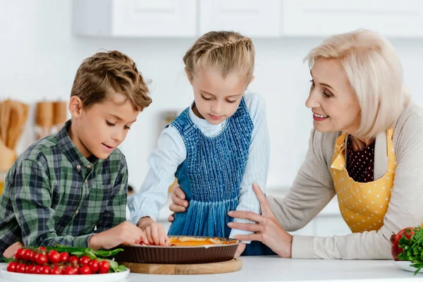 Adorables hermanos haciendo pastel y divertirse con la abuela en la cocina - foto de stock