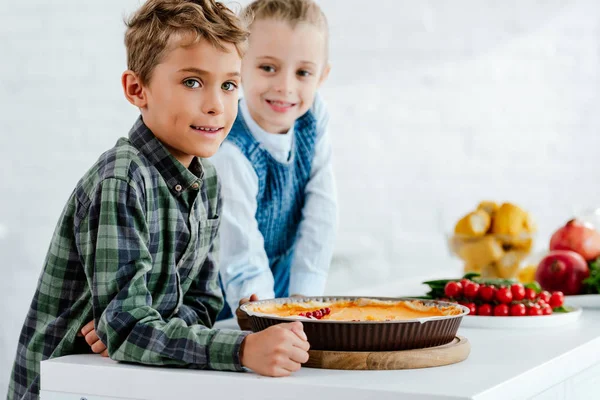 Siblings with pumkin pie looking at camera together at kitchen — Stock Photo