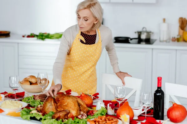 Senior femme servir table pour thanksgiving dîner dans la cuisine à la maison — Photo de stock