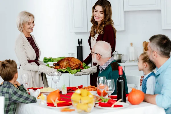 Усміхнені жінки носять смачну запечену індичку для подячної вечері з великою сім'єю — стокове фото