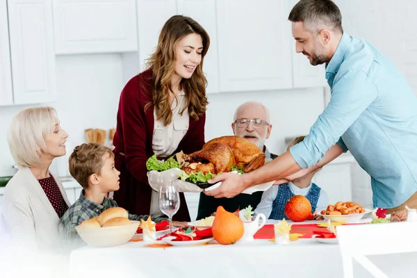 Couple adulte portant dinde cuite au four pour le dîner de Thanksgiving avec une grande famille — Photo de stock