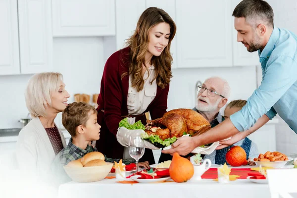 Happy adult couple carrying baked turkey for thanksgiving dinner with big family at home — Stock Photo