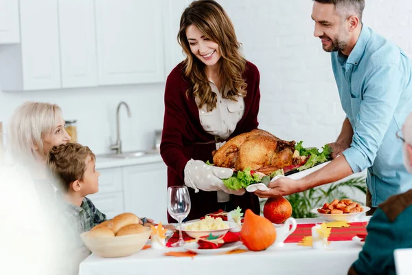 Smiling adult couple carrying baked turkey for thanksgiving dinner with big family — Stock Photo