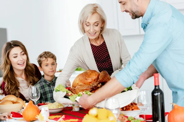 Happy senior woman and adult man carrying baked turkey for thanksgiving dinner with family — Stock Photo