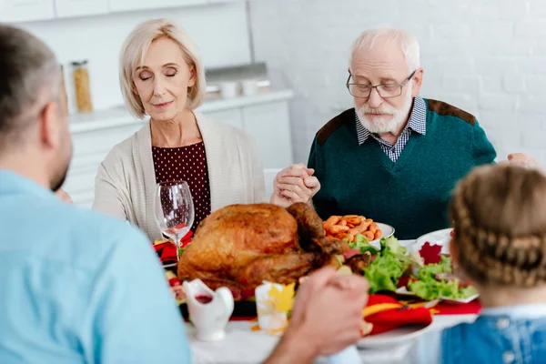 Coppia anziana con la famiglia che prega al tavolo servito con tacchino prima della cena di festa il Ringraziamento — Foto stock