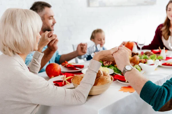 Семья, держась за руки и молясь вместе перед праздничным ужином за столом с индейкой — стоковое фото
