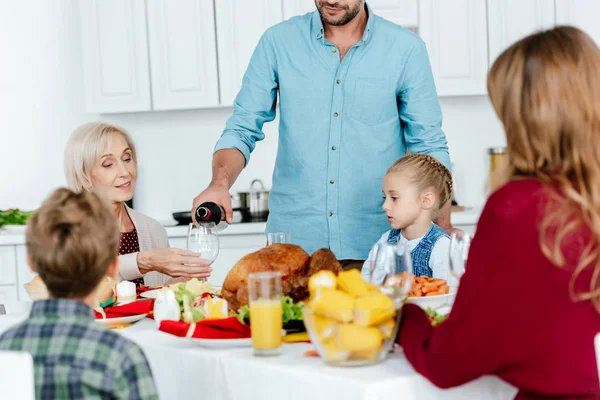 Visão parcial do homem derramando vinho em vidro, enquanto a família celebrando ação de graças na mesa servida com peru assado — Fotografia de Stock