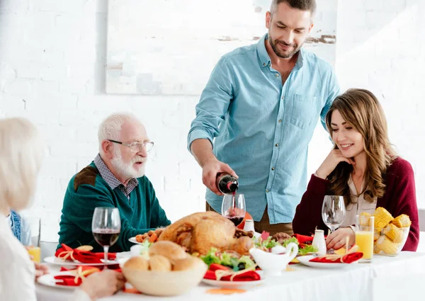 Homme adulte verser du vin dans le verre à la table servie tandis que la famille ayant fête d'action de grâces à la maison — Photo de stock