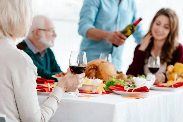 Seniorin mit Weinglas feiert Erntedank mit Familie am Serviertisch mit Truthahn — Stockfoto