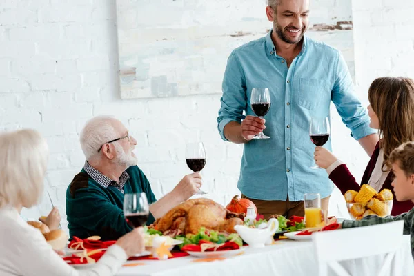 Счастливый взрослый мужчина с бокалом вина делает тост в то время как его семья празднует ужин на День Благодарения — стоковое фото