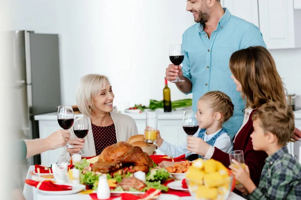 Teilansicht eines erwachsenen Mannes mit Weinglas, der am Tisch mit Truthahn anstößt, während seine Familie Erntedank feiert — Stockfoto