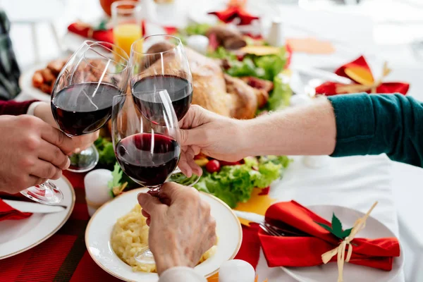 Imagen recortada de la familia tintineo por copas de vino mientras se celebra el día de acción de gracias en la mesa servida con pavo al horno - foto de stock