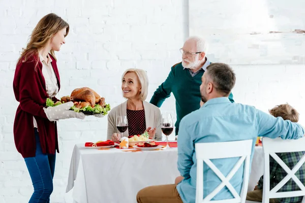 Heureuse femme adulte portant dinde cuite au four pour le dîner de Thanksgiving avec la famille — Photo de stock