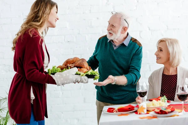 Attractive adult woman carrying turkey for thanksgiving celebration with senior parents — Stock Photo