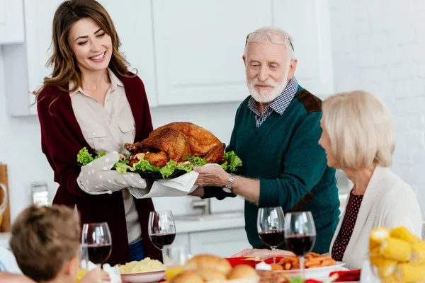 Пожилой мужчина и взрослая женщина несут запечённую индейку на ужин в честь Дня Благодарения с семьей дома — стоковое фото