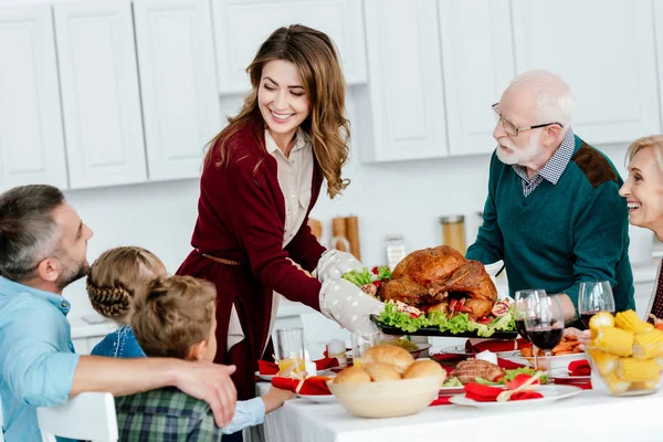 Happy adult woman and senior man carrying baked turkey for thanksgiving celebration with family at home — Stock Photo