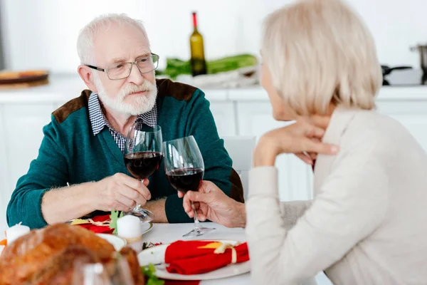 Couple sénior cliquetis par des verres à vin à la table de service avec dinde cuite au four sur thanksgiving — Photo de stock