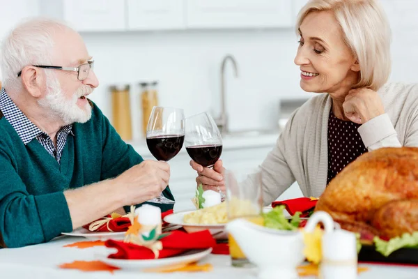 Sorrindo casal sênior clinking por copos de vinho na mesa de servir com peru assado em ação de graças — Fotografia de Stock