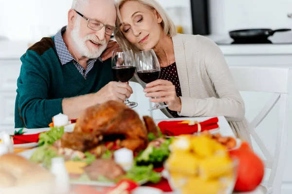 Heureux couple sénior cliquetis par verres à vin à servir table avec dinde cuite au four sur thanksgiving — Photo de stock