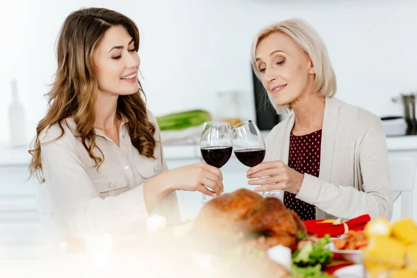 Bela mulher adulta clinking por copos de vinho com mãe sênior na mesa servida para a celebração de ação de graças — Fotografia de Stock