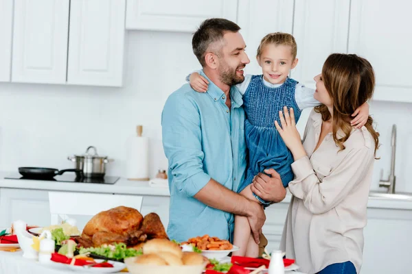 Família feliz segurando pequena filha perto da mesa servida para o jantar de ação de graças — Fotografia de Stock