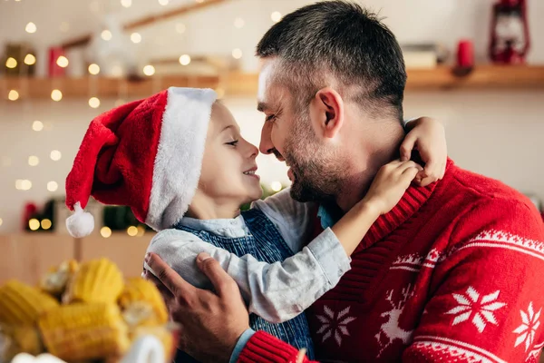 Side view of happy father and little daughter in christmas hat face to face at table with holiday dinner — Stock Photo