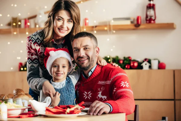 Portrait of happy family with daughter in christmas hat sitting at table with holiday dinner — Stock Photo