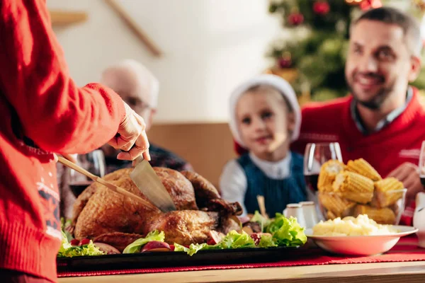 Zugeschnittenes Bild einer Frau, die köstlichen Tukey für das Weihnachtsessen mit glücklicher Familie zu Hause schneidet — Stockfoto