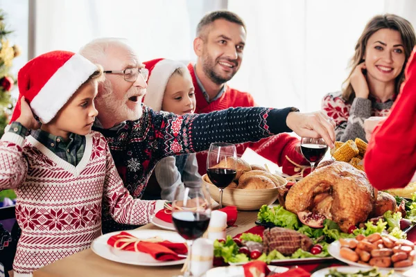 Happy senior man pointing at turkey while having christmas dinner with family at home — Stock Photo