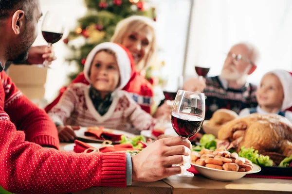 Vista parcial del hombre con el vino sentado en la mesa con la familia durante la cena de Navidad - foto de stock