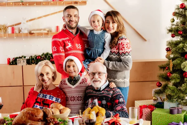 Familia feliz con niños pequeños en sombreros de Navidad sentados en la mesa durante la cena de Navidad en casa - foto de stock