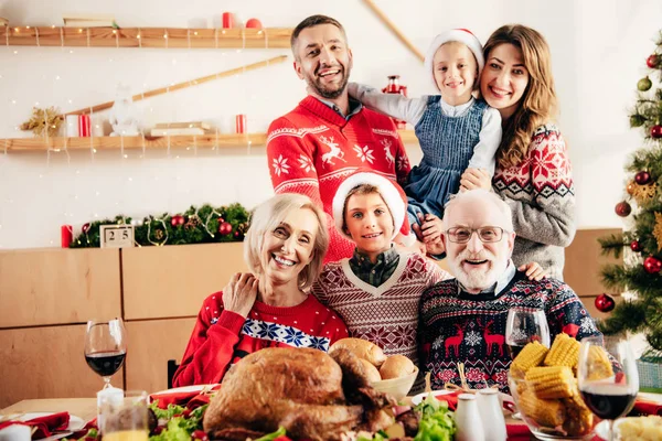 Glückliche Familie mit kleinen Kindern in Weihnachtsmützen am Tisch beim Weihnachtsessen zu Hause — Stockfoto