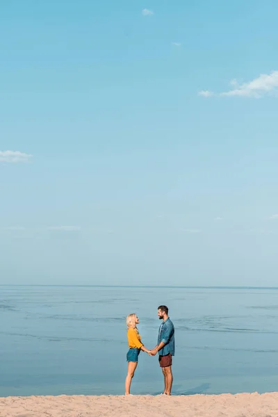 Pareja cogida de la mano y mirándose en la playa - foto de stock