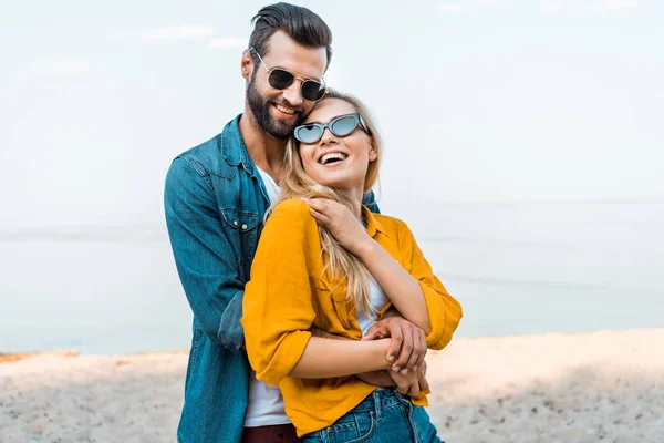 Парень обнимает смеющуюся девушку на пляже — стоковое фото
