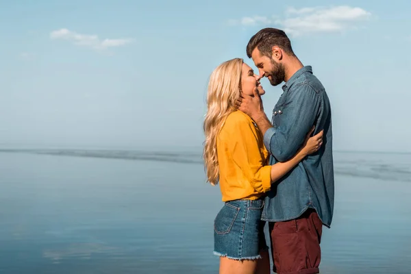 Vista lateral de namorada sorridente e namorado tocando com narizes na praia — Fotografia de Stock