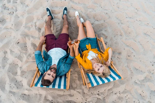 High angle view of couple lying on sun loungers with beer in bottles on sandy beach — Stock Photo